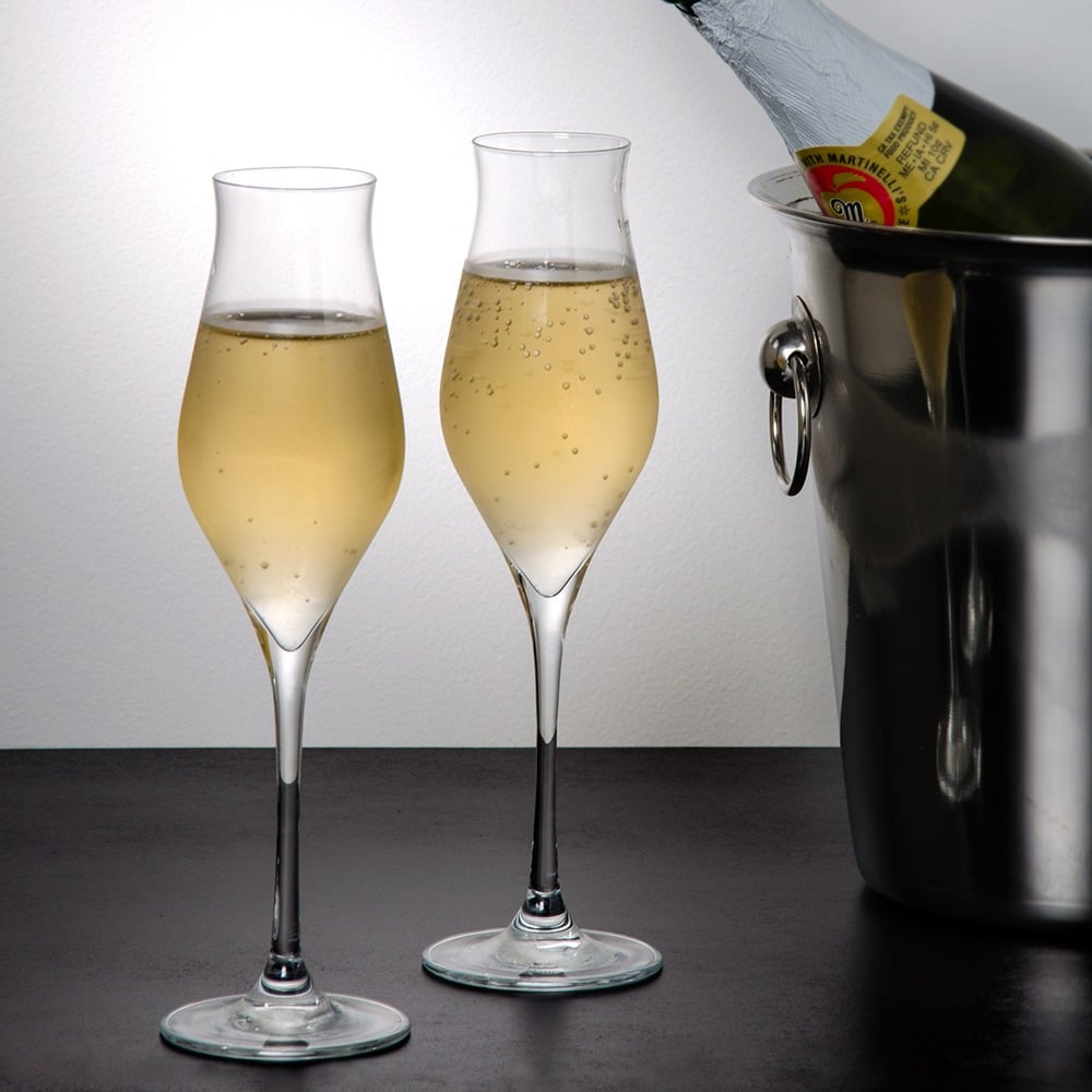 Two tulip wine glasses filled with sparkling wine in front of a stainless steel wine cooler