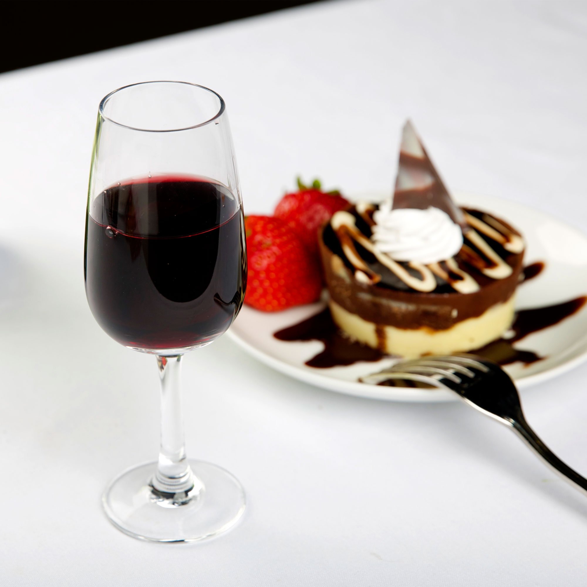Dessert wine glass filled with port in front of an elegant dessert, complete with fresh strawberries