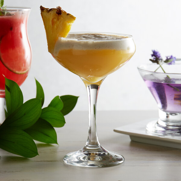 Coupe wine glass filled with a fruity drink, garnished with a slice of fresh pineapple