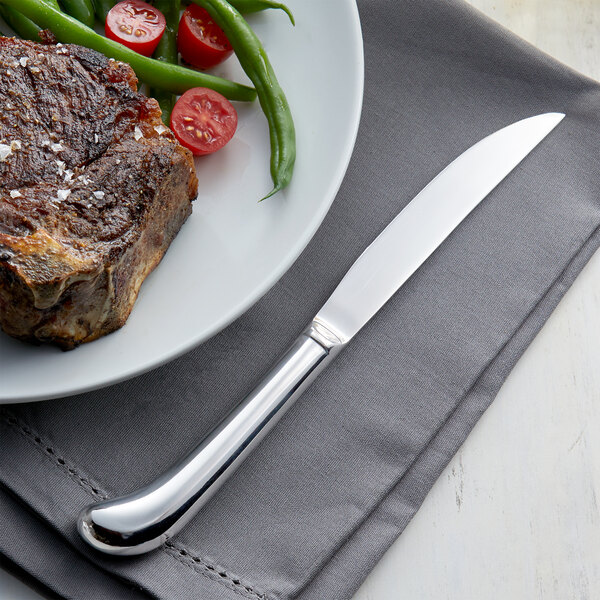 Steak knife on gray napkin next to plate with steak, green beans, and cherry tomatoes