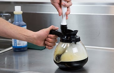 scrubbing a coffee pot with a brush