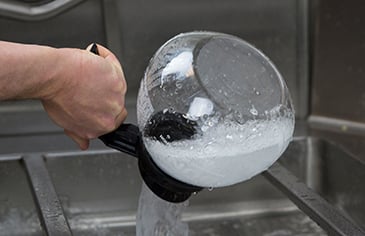 soapy water contents being poured out of a coffee pot and into a sink