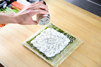 sprinkling sesame seeds on uramaki