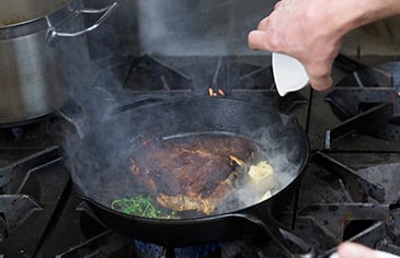 adding aromatics and butter to steak in a cast iron skillet
