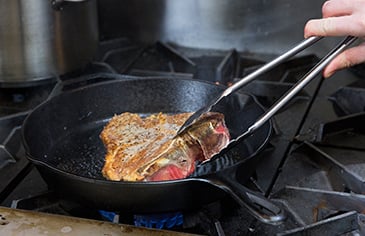 flipping a steak in a cast iron skillet