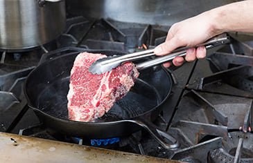 Placing a raw steak onto a cast iron skillet