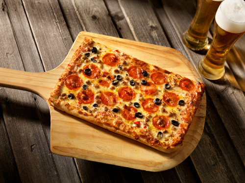 Sicilian pizza on pizza peel with beers next to it