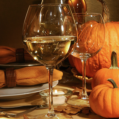 glass of white wine next to empty glasses and pumpkins
