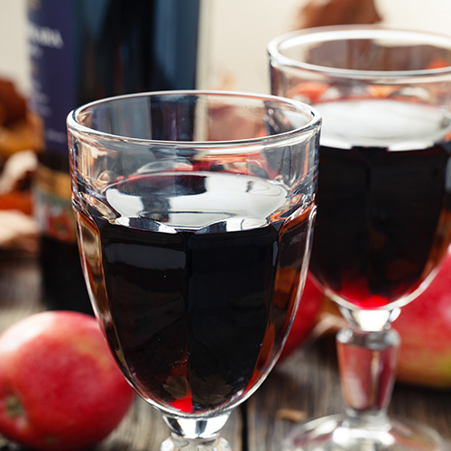 two glasses of red wine with wine bottle and apples behind