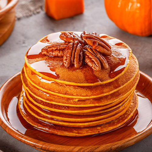 stack of pancakes with maple syrup and pecans on top