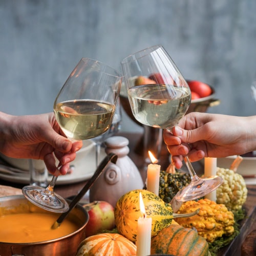 two hands clinking glasses of white wine over Thanksgiving dinner