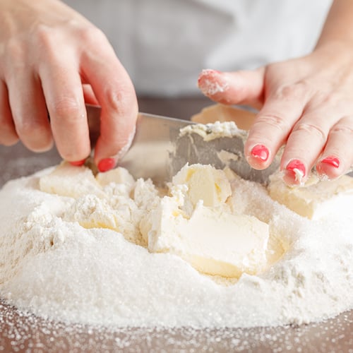 hands using a knife to cut shortening into a pile of flour