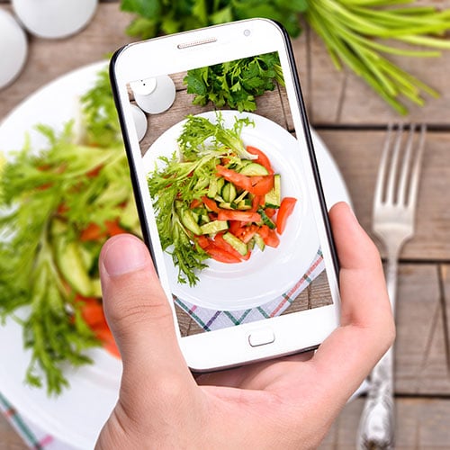 Hand holding iPhone taking photo of plate of vegetables for Instagram marketing