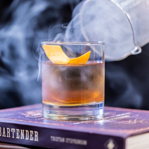 glass of smoking whiskey on top of bartender manual book