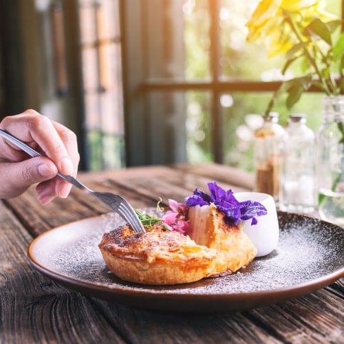 hand putting fork into molecular gastronomy pastry with purple flower on wooden table