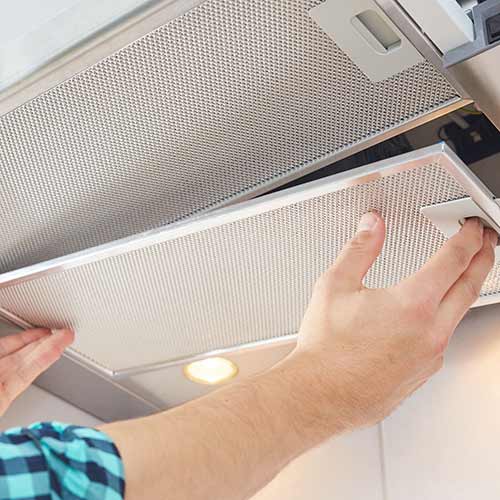hands removing a filter from cooker hood for cleaning or service