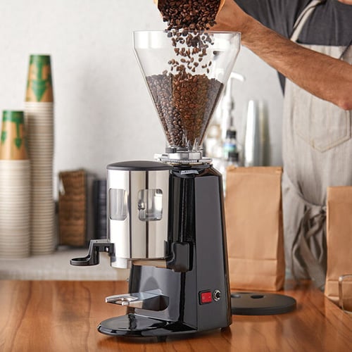 person pouring fresh coffee beans into coffee grinder