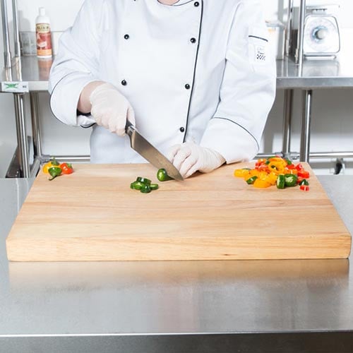 chef in white coat cutting multi colored peppers with large knife