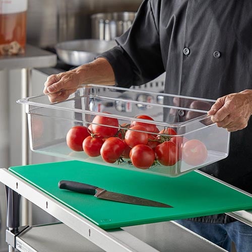 kitchen staff member wearing gray chef coat holding a clear plastic bin filled with tomatoes