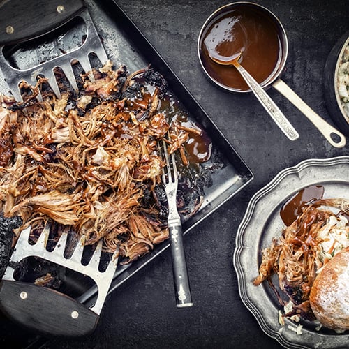 top view of shredded barbecue on black slate background with coleslaw and artisan bun
