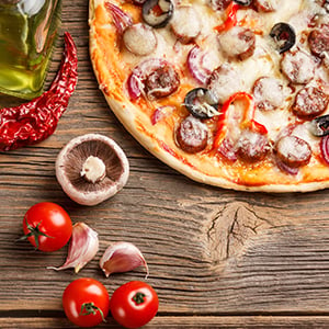 California pizza on wooden table with tomatoes, garlic, mushroom, and pepper next to it 