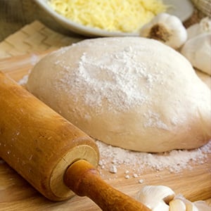 Pizza dough on a cutting board next to rolling pin