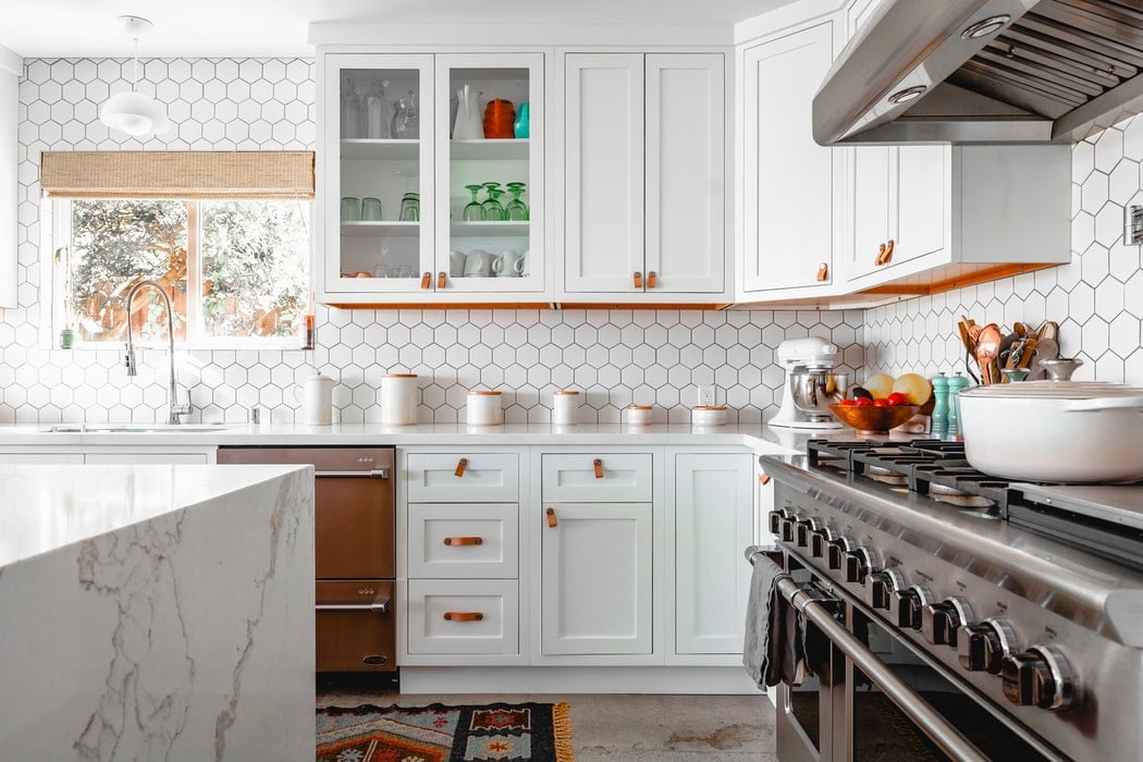 Airbnb kitchen with a stovetop, white cabinets, marble countertop, and a tile backsplash