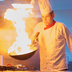 male chef handling large pan with flames