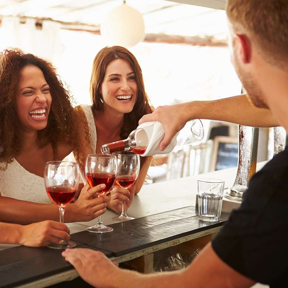 bar tender pouring red wine for two women