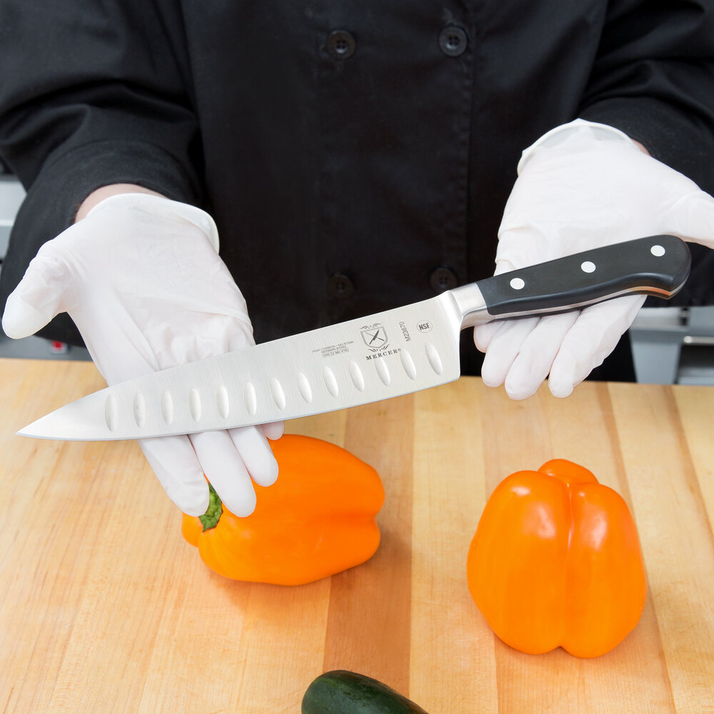 Hands holding large forged knife above cutting board with orange bell peppers