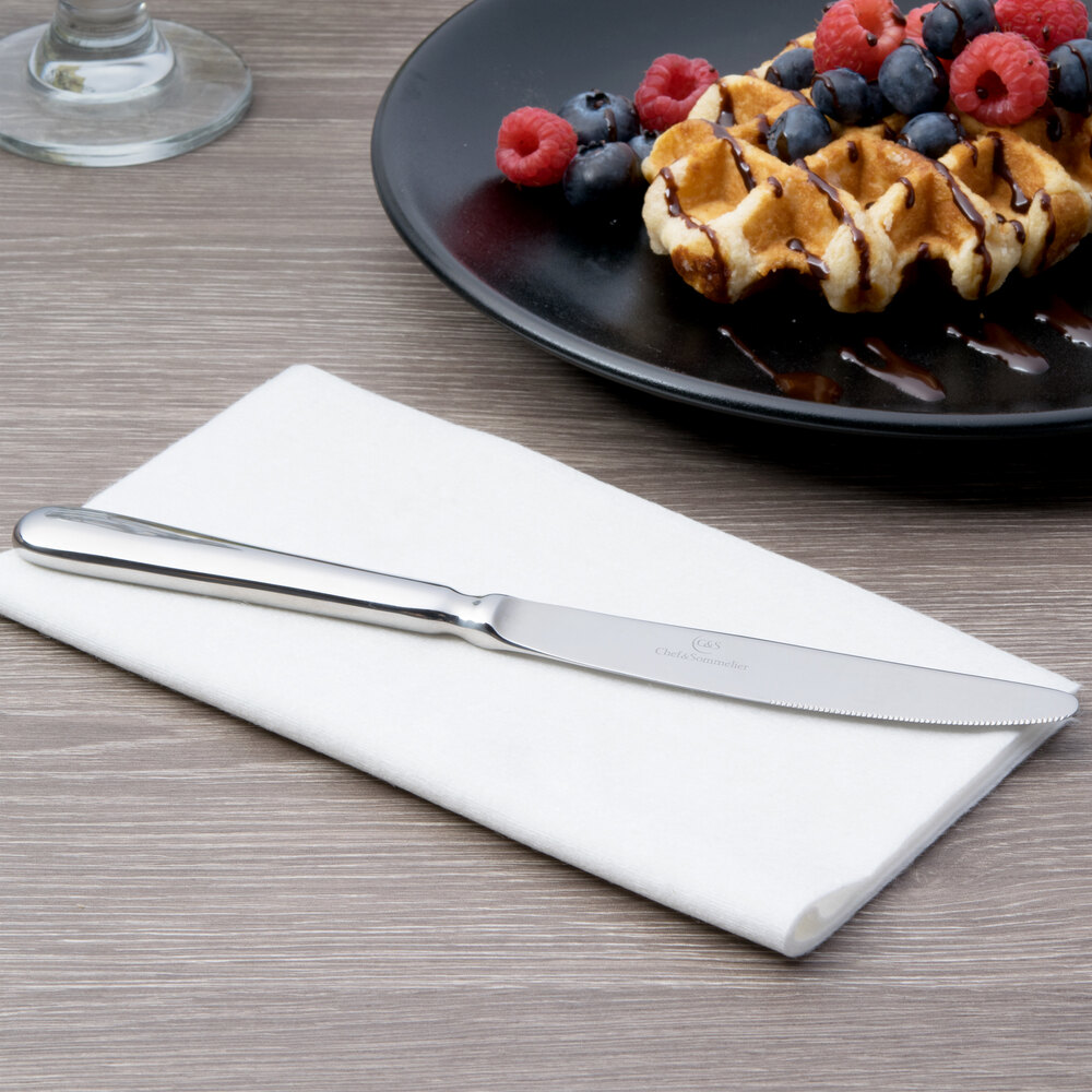Dessert knife on white napkin next to plate of waffles