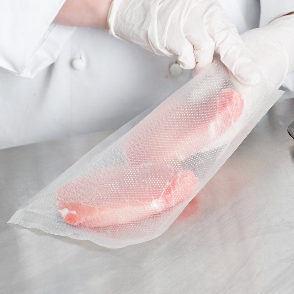 Gloved hands placing two raw pork chops into bag for vacuum sealing
