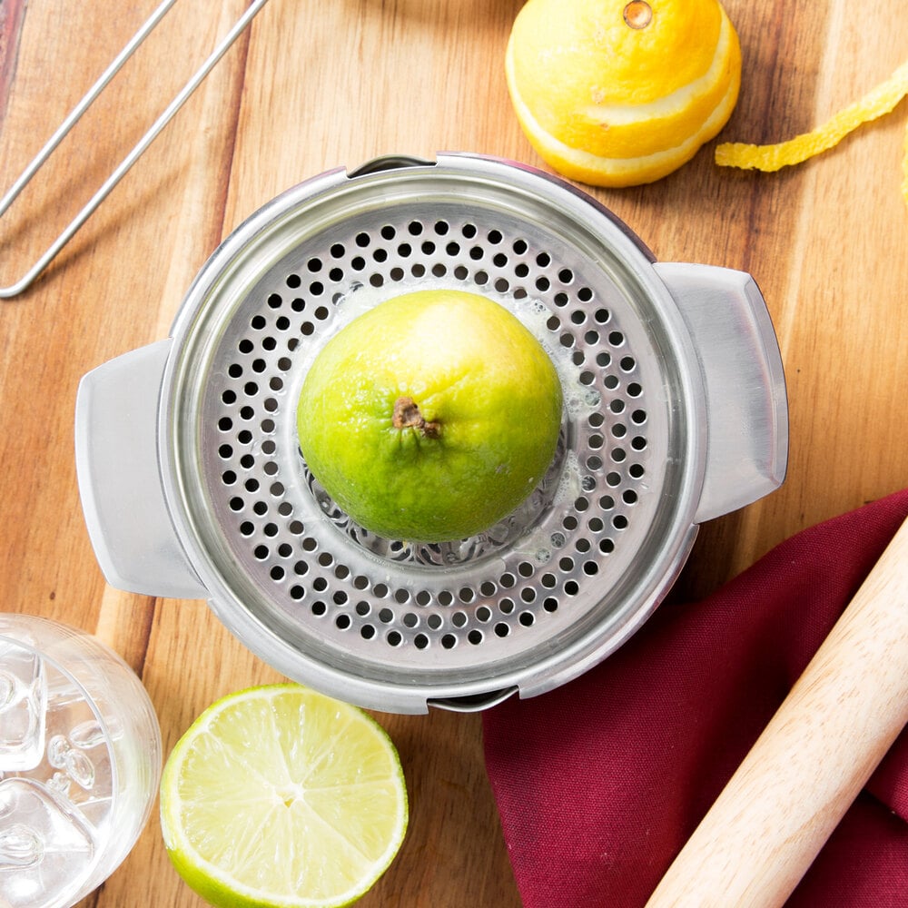 Squeezing a lime with a stainless steel citrus reamer on a wooden table