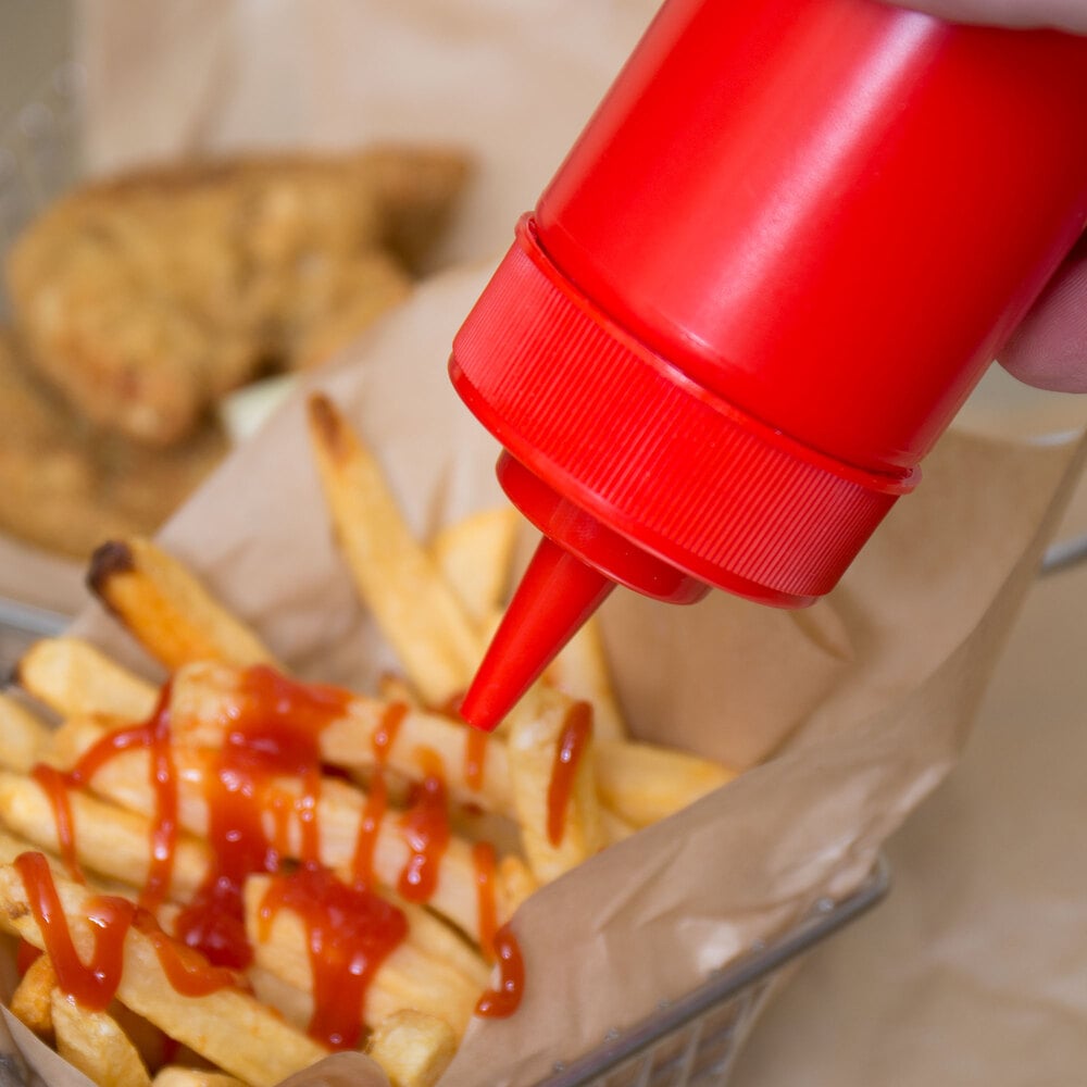 Red bottle of ketchup being squeezed on top of a basket of french fries