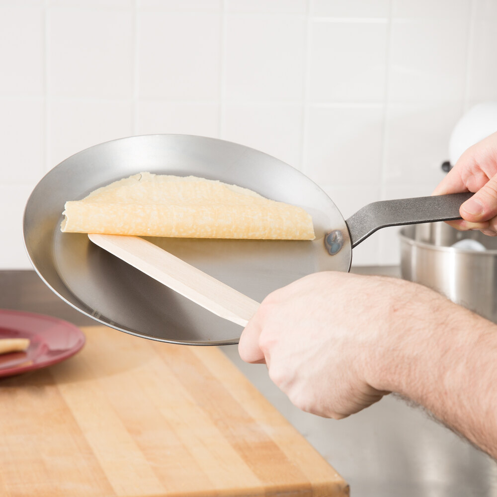 Wood spreader spreading crepe batter over a crepe pan