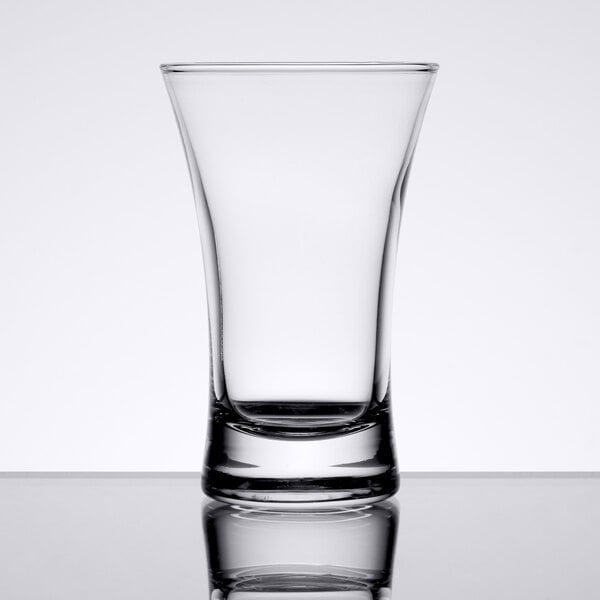 An Arcoroc clear shot glass on a reflective surface.