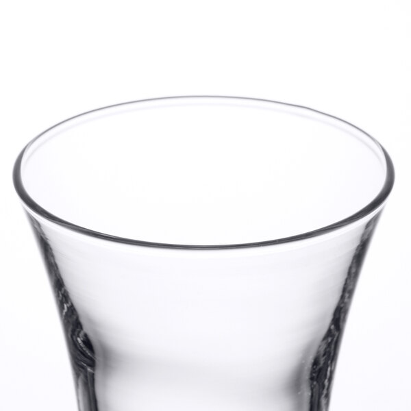 An Arcoroc shot glass with a small amount of liquid in it.