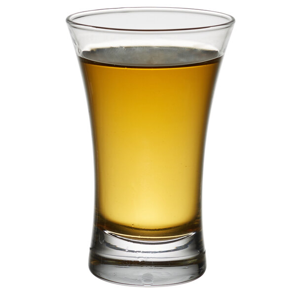 An Arcoroc shot glass filled with amber liquid on a white background.