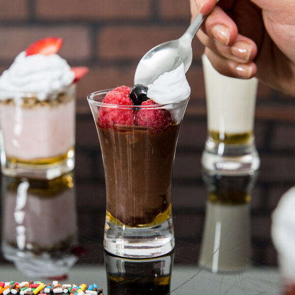 A person holding an Arcoroc shot glass with a brown liquid in it.