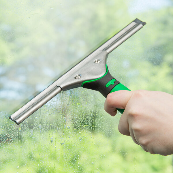 A hand using a Unger squeegee with a green handle to clean a window.