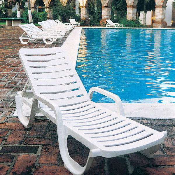 A group of white Grosfillex Bahia chaise lounges next to a pool.