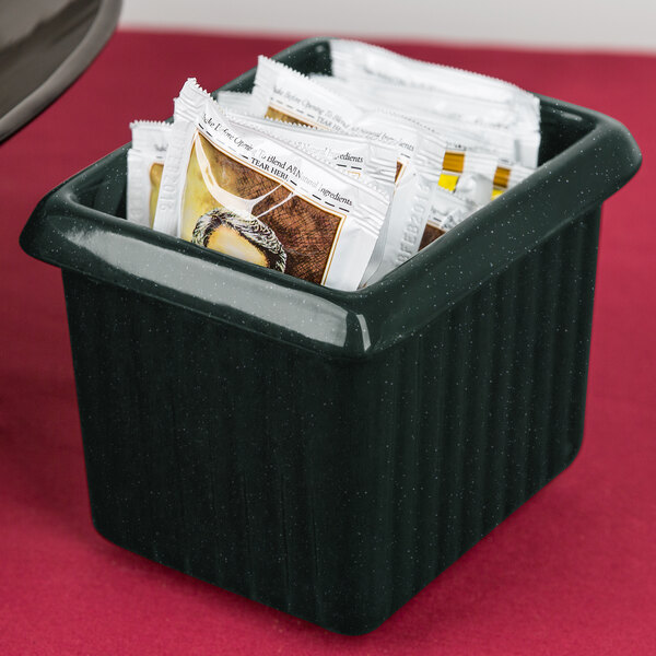 A hunter green rectangular server with white speckles holding packets of sugar on a hotel buffet counter.