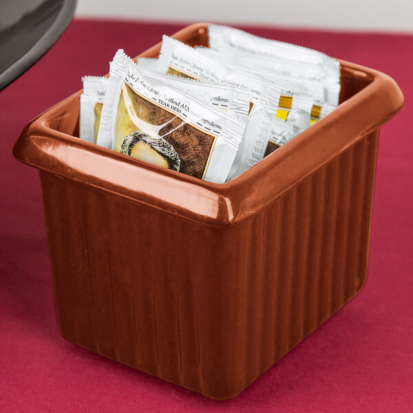 A Tablecraft copper cast aluminum rectangle server with tea packets in it on a hotel buffet counter.