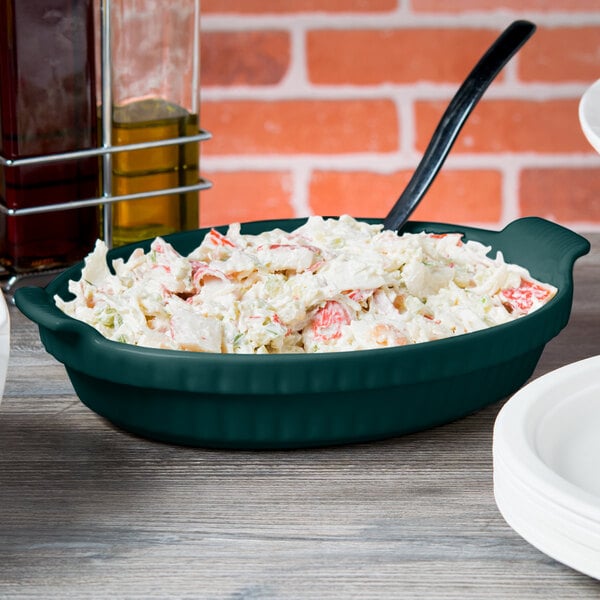 A Tablecraft hunter green shallow oval casserole dish filled with food on a table.