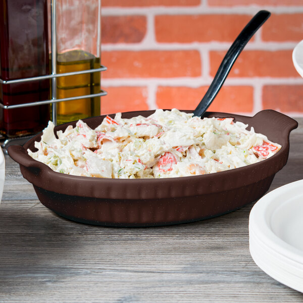 A Tablecraft Midnight Speckle shallow oval casserole dish filled with food on a table.