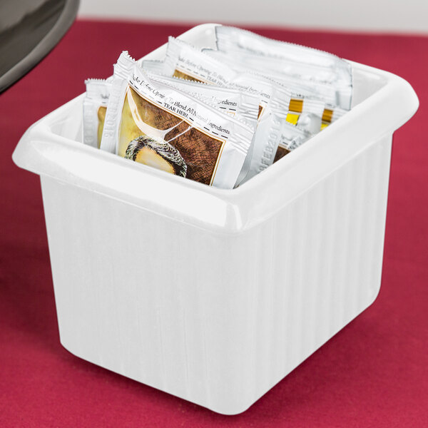 A Tablecraft white cast aluminum rectangle server with ridges holding packets.