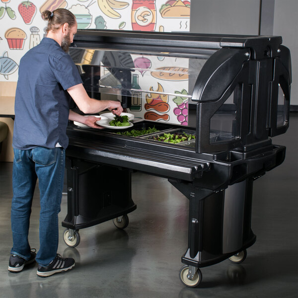A man standing next to a Cambro Versa Bar with a sneeze guard panel on it.
