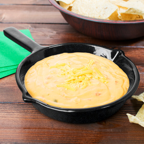 A Tablecraft Midnight with Blue Speckle cast aluminum fry pan of cheese dip next to a bowl of chips.