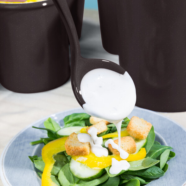 A Tablecraft Midnight Speckle long ladle pouring dressing over a salad.