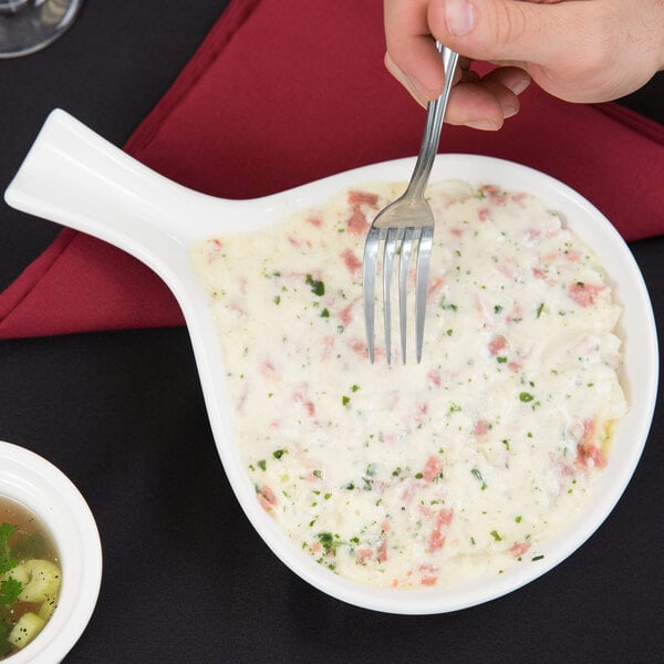 A person holding a Tuxton white china fry pan server with food in it.